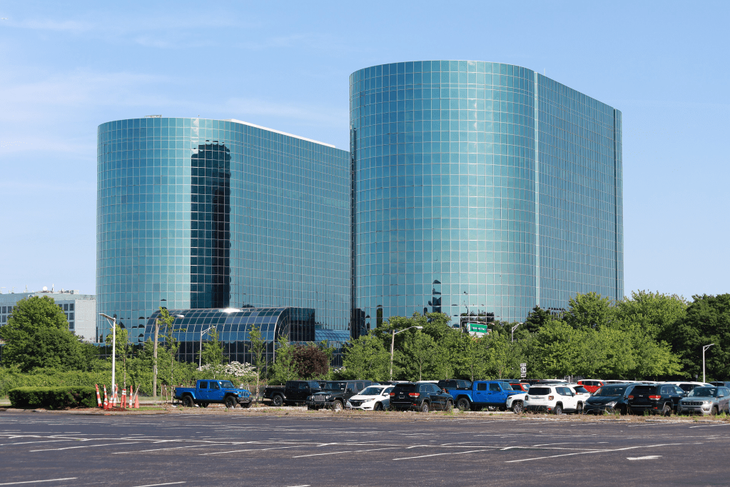 Two glass office buildings with rounded fronts that reflect the parking lot surrounding them.